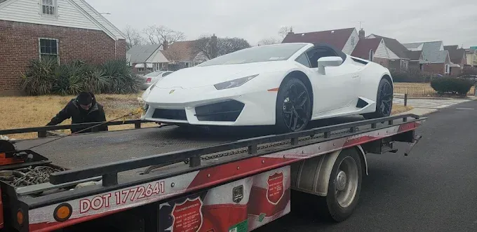 White Lamborghini convertible being towed by a tow truck on a residential street.