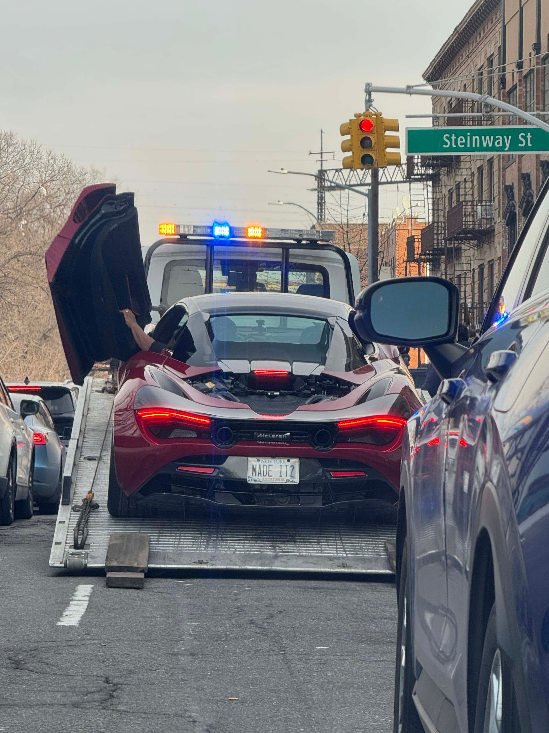 A red sports car with its rear hatch open at a police stop on a city street, near a sign reading “S W 1st St.”
