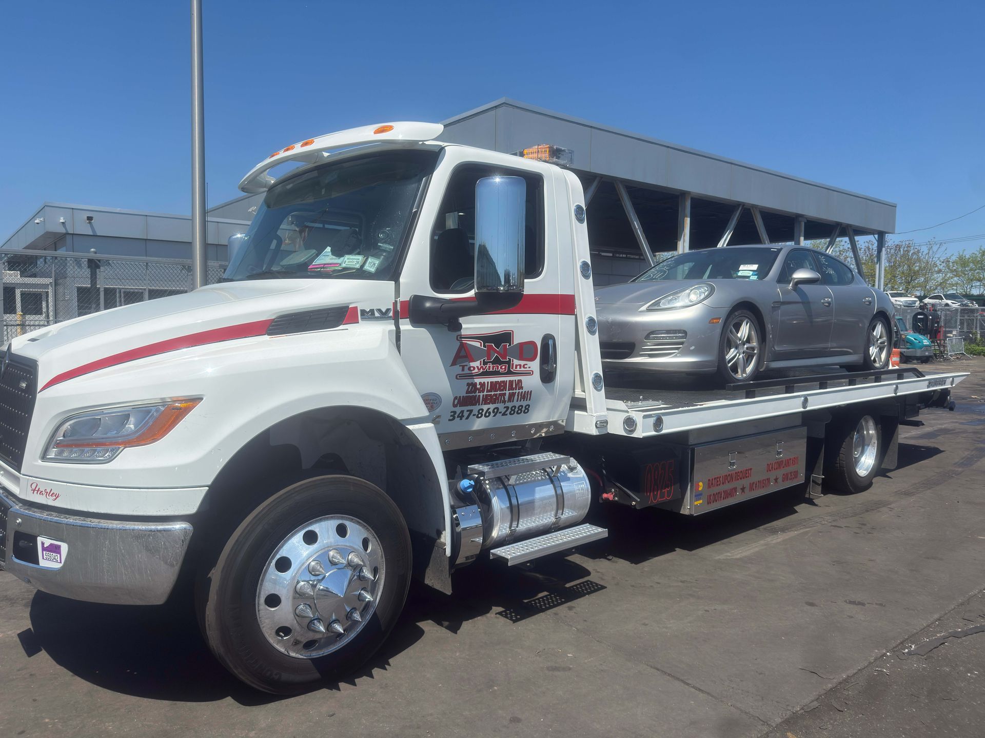 White tow truck carrying a gray sedan on a flatbed in a sunny parking lot