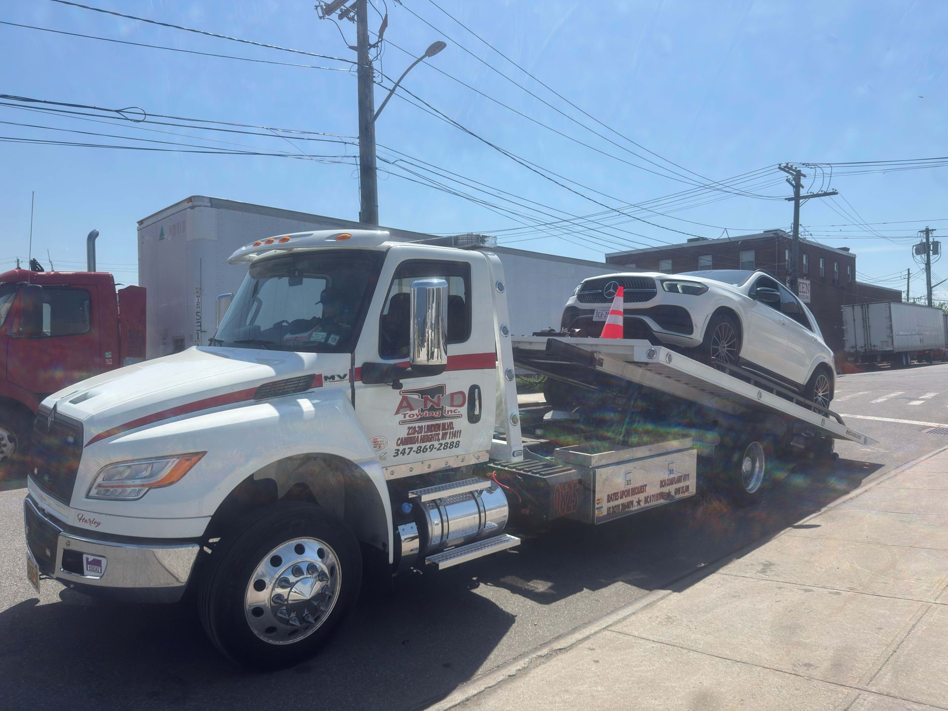 Tow truck loading a white car on a flatbed beside a street under a bright blue sky