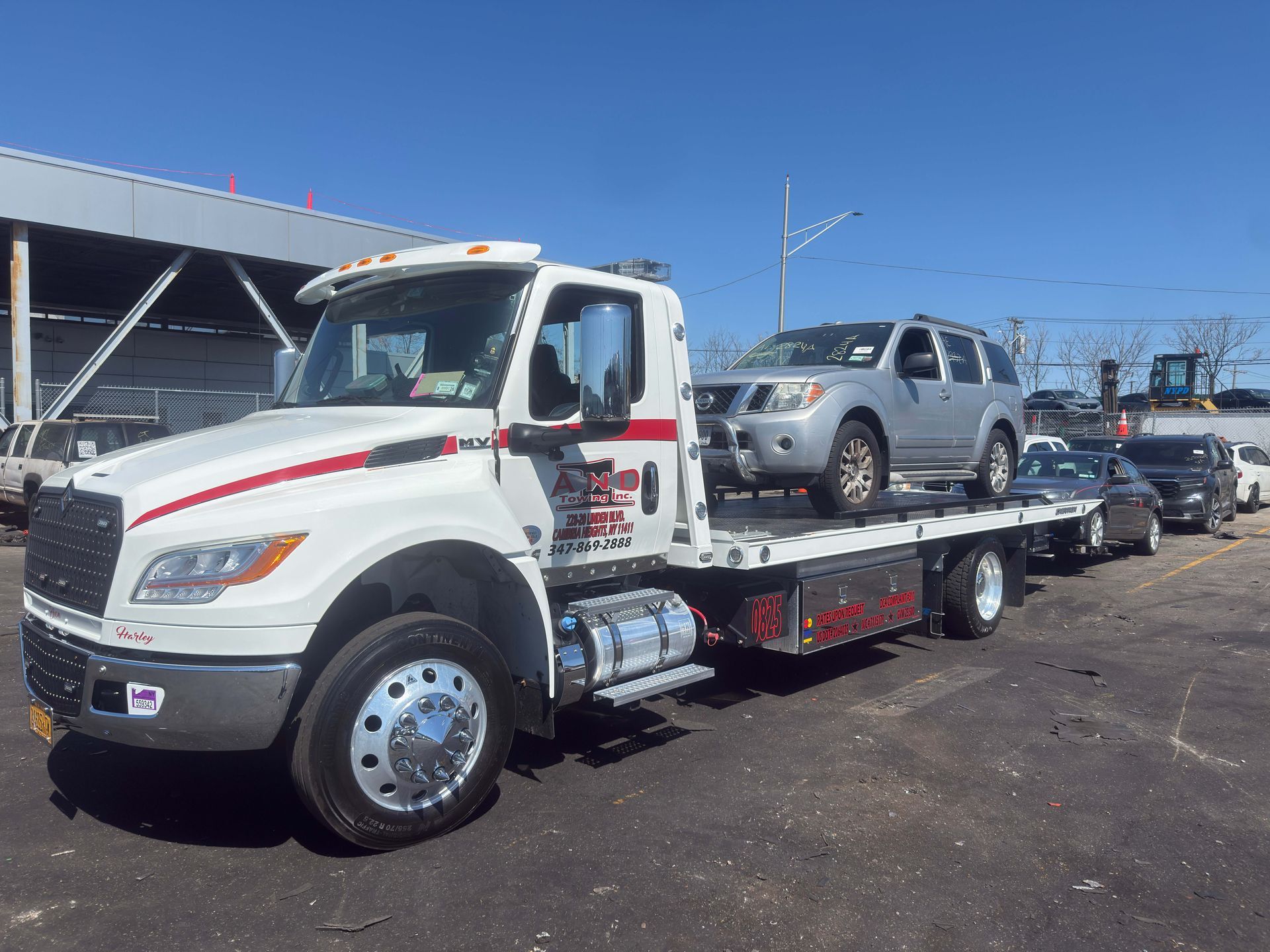 White tow truck carrying a silver pickup on a flatbed in a sunny parking lot