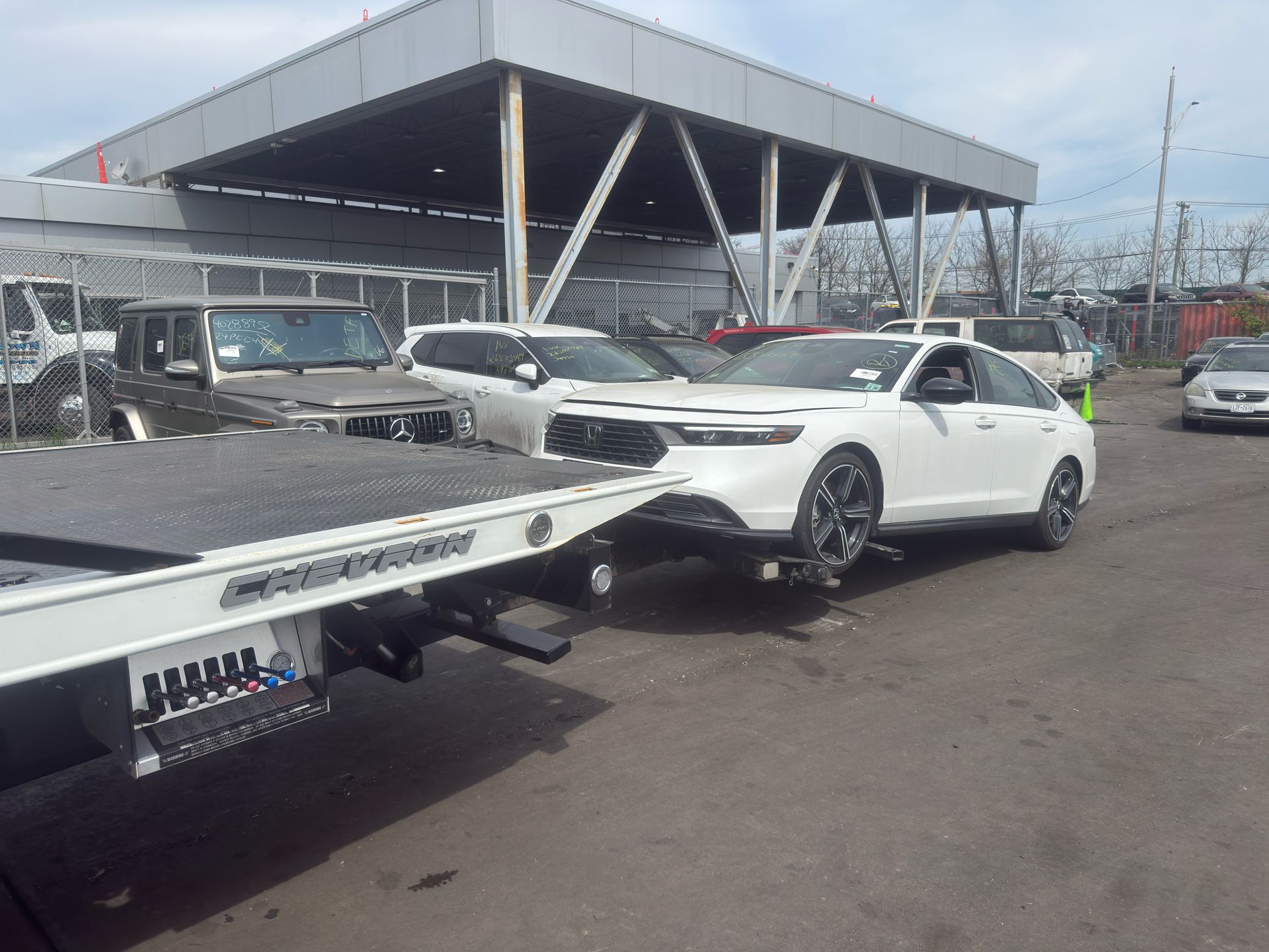 White sports car on a flatbed tow truck in a parking lot near a large canopy structure