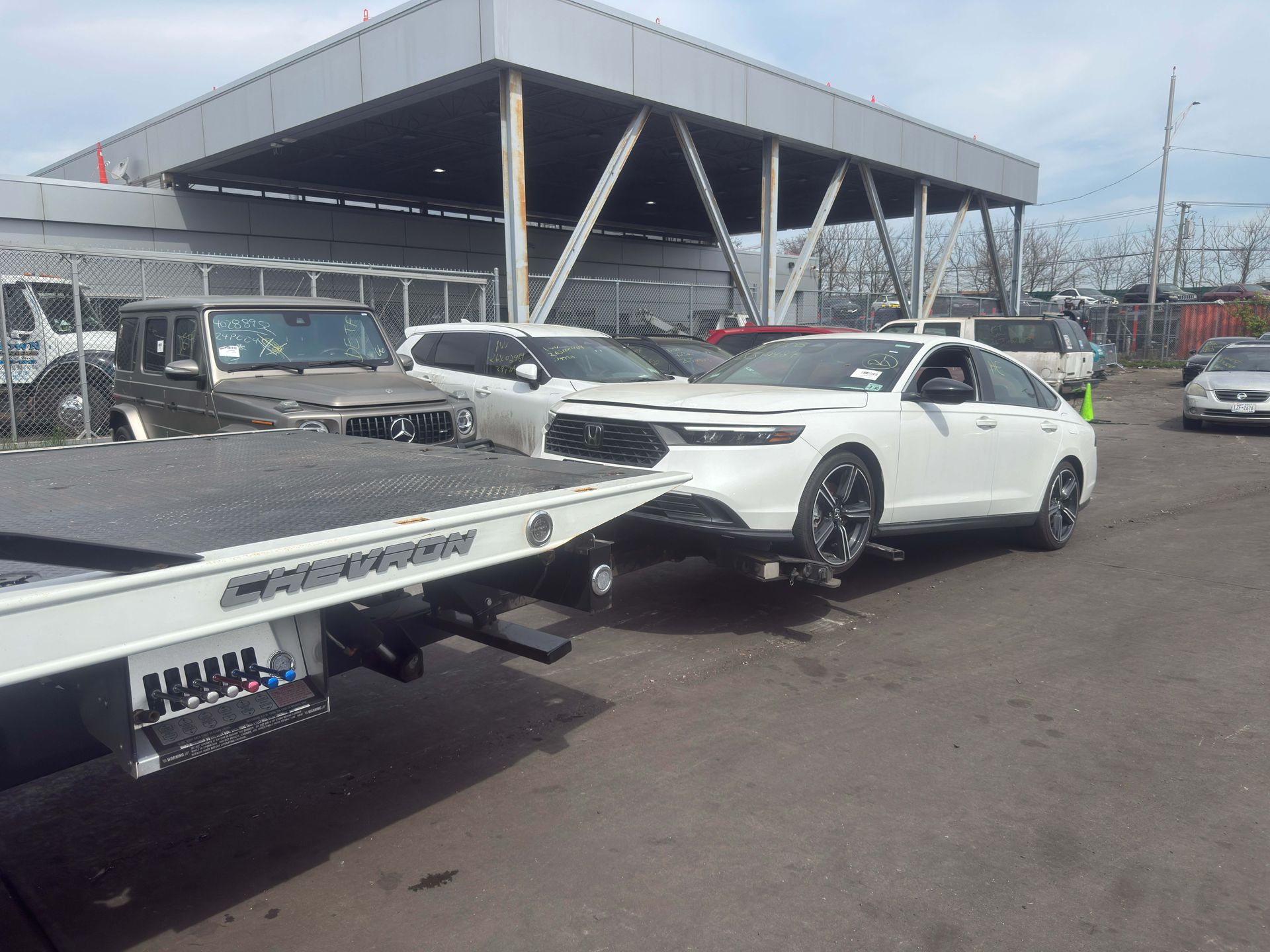 White sports car on a tow truck in a parking lot outside a dealership.