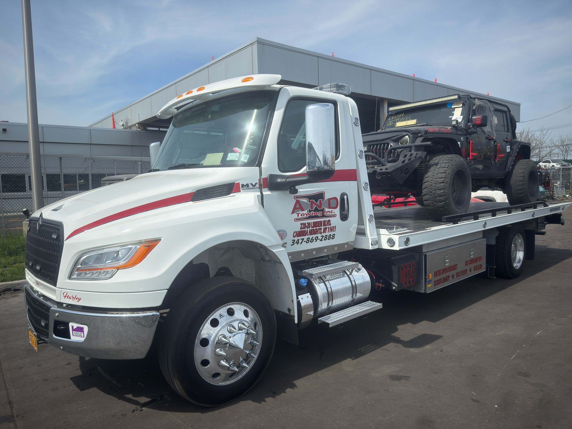 White flatbed tow truck hauling a black off-road vehicle in a parking lot.