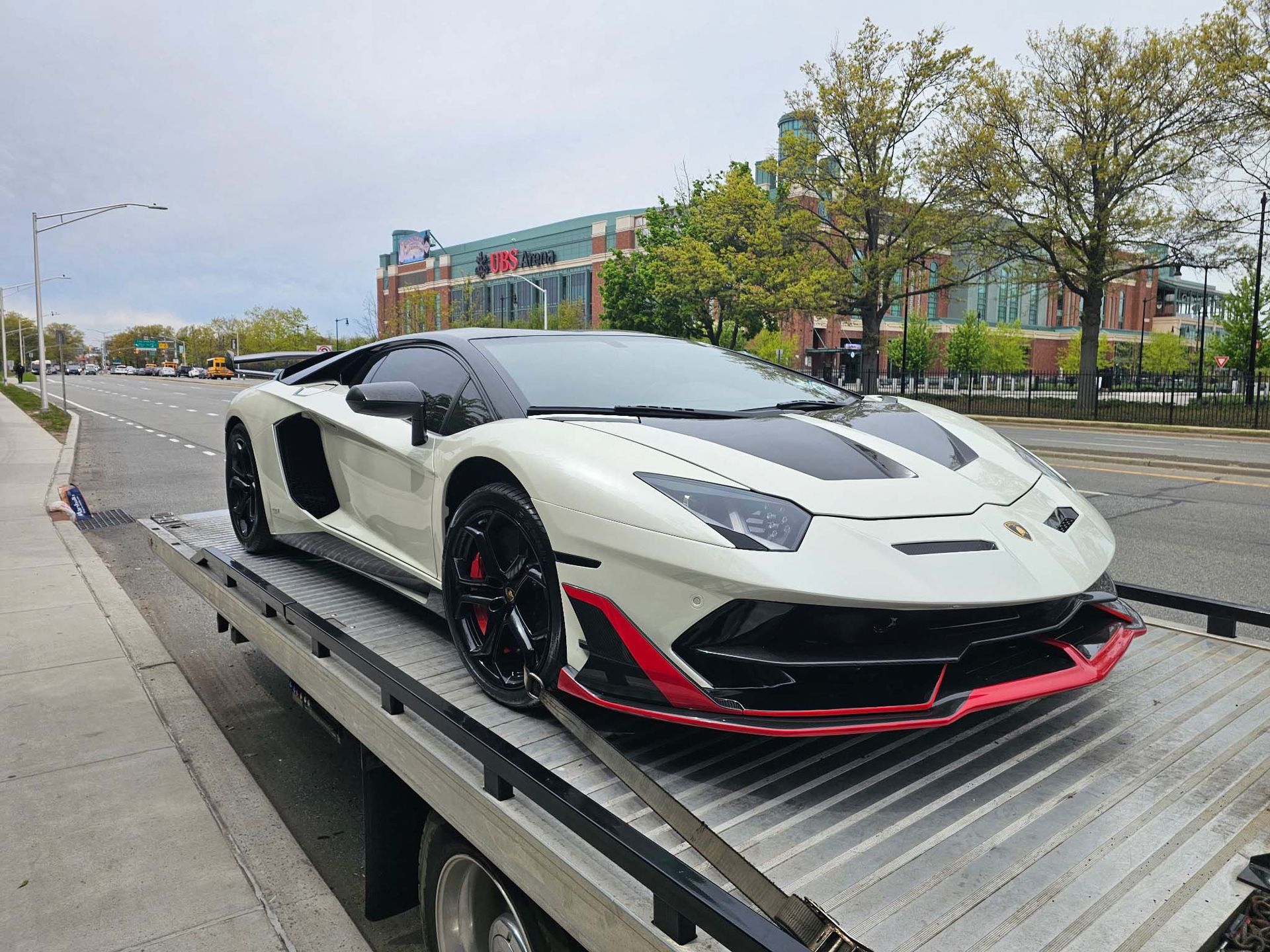 White sports car on a flatbed tow truck beside a road on a cloudy day