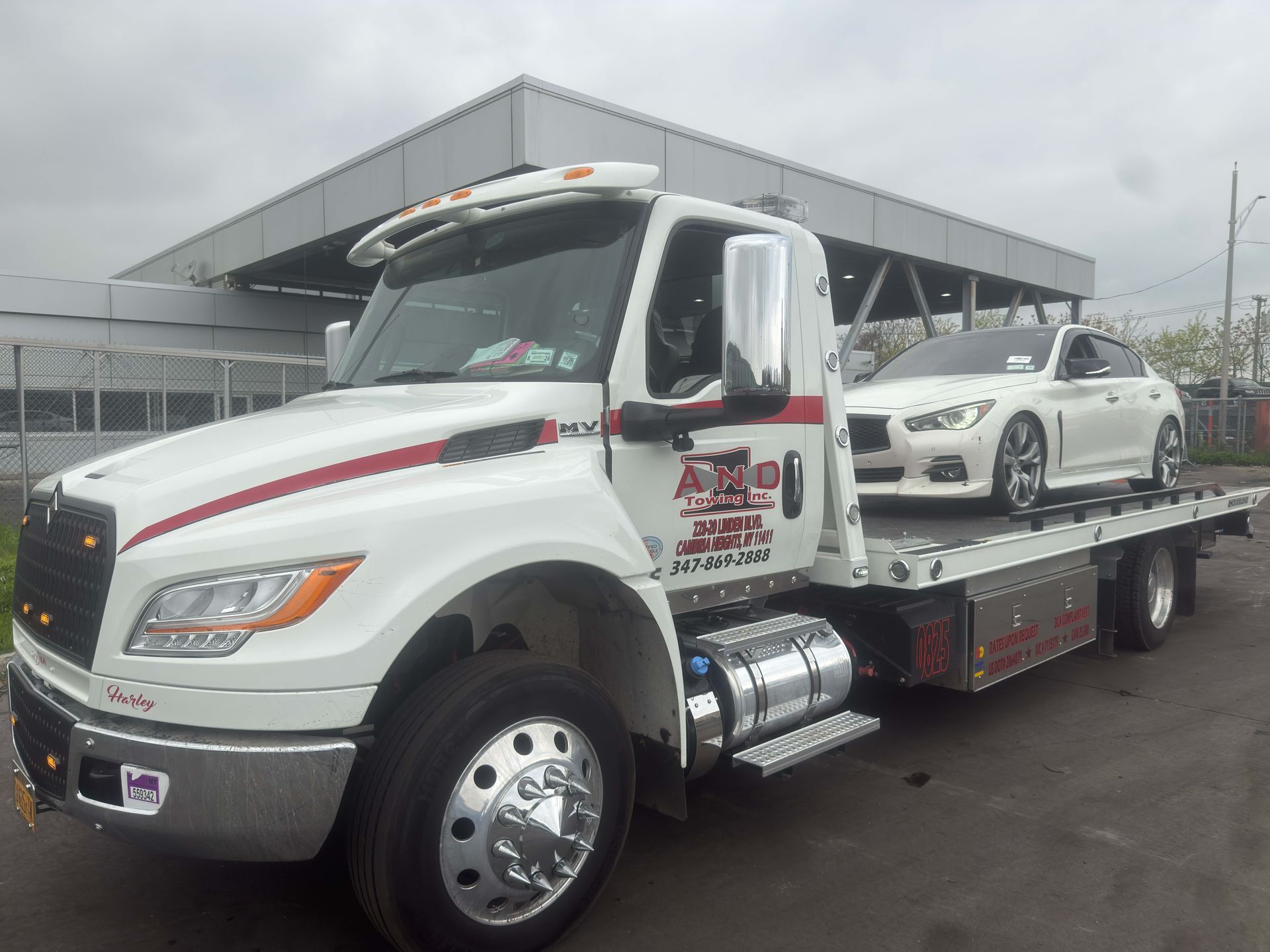 White tow truck hauling a white car on a flatbed in a parking lot