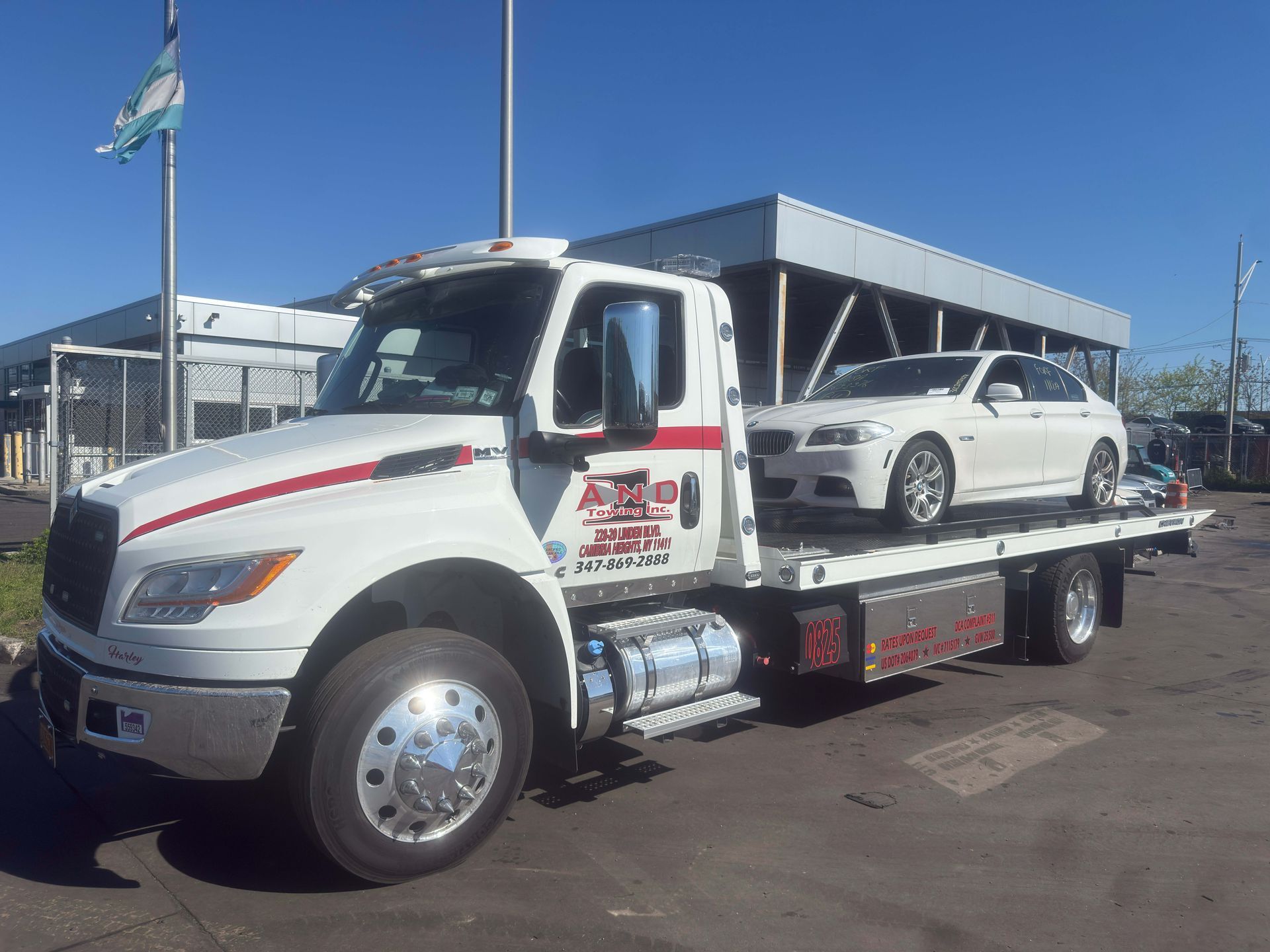 White tow truck carrying a white car on a flatbed in a sunny parking lot