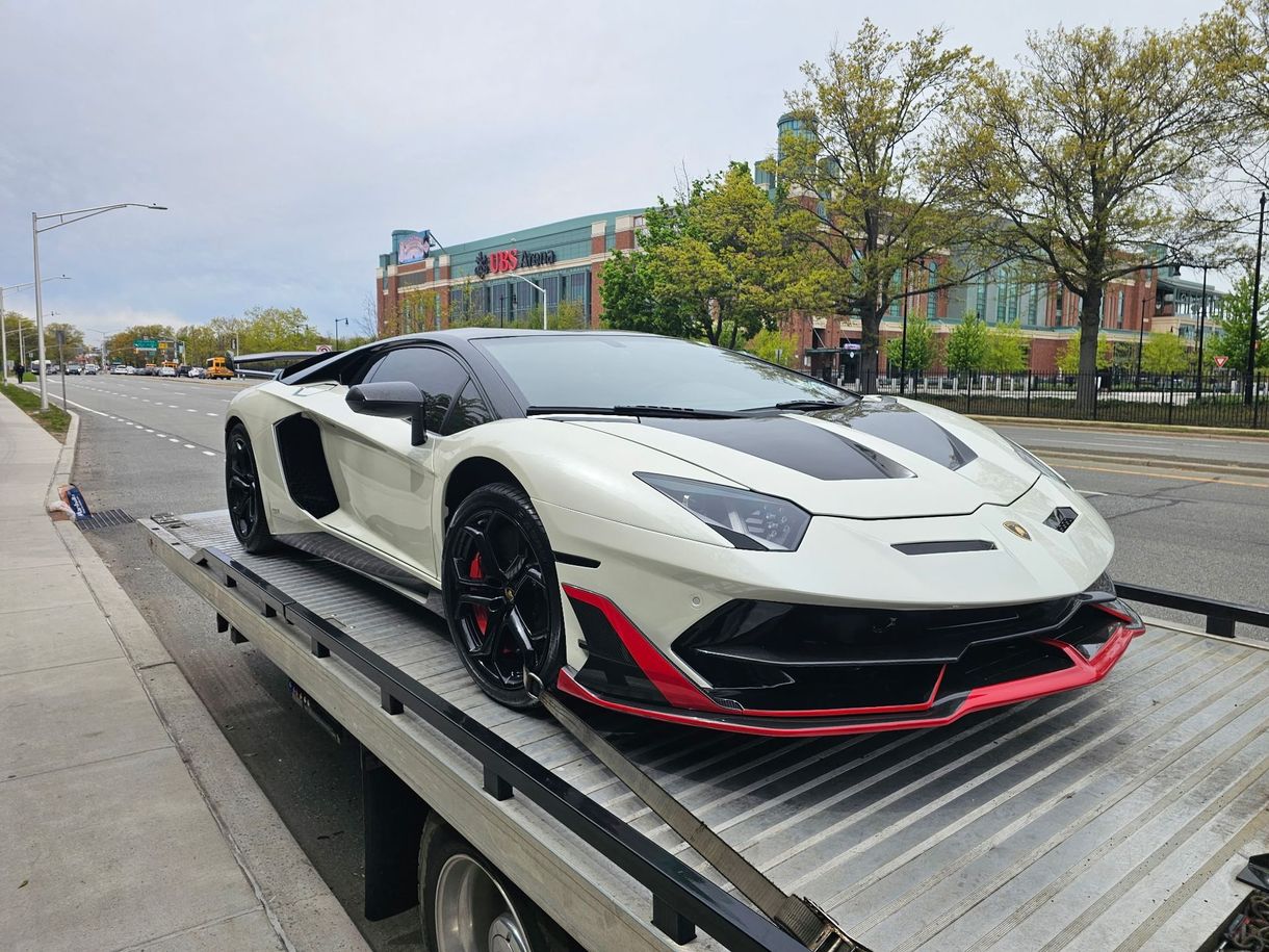 White and black sports car on a flatbed tow truck beside a city street