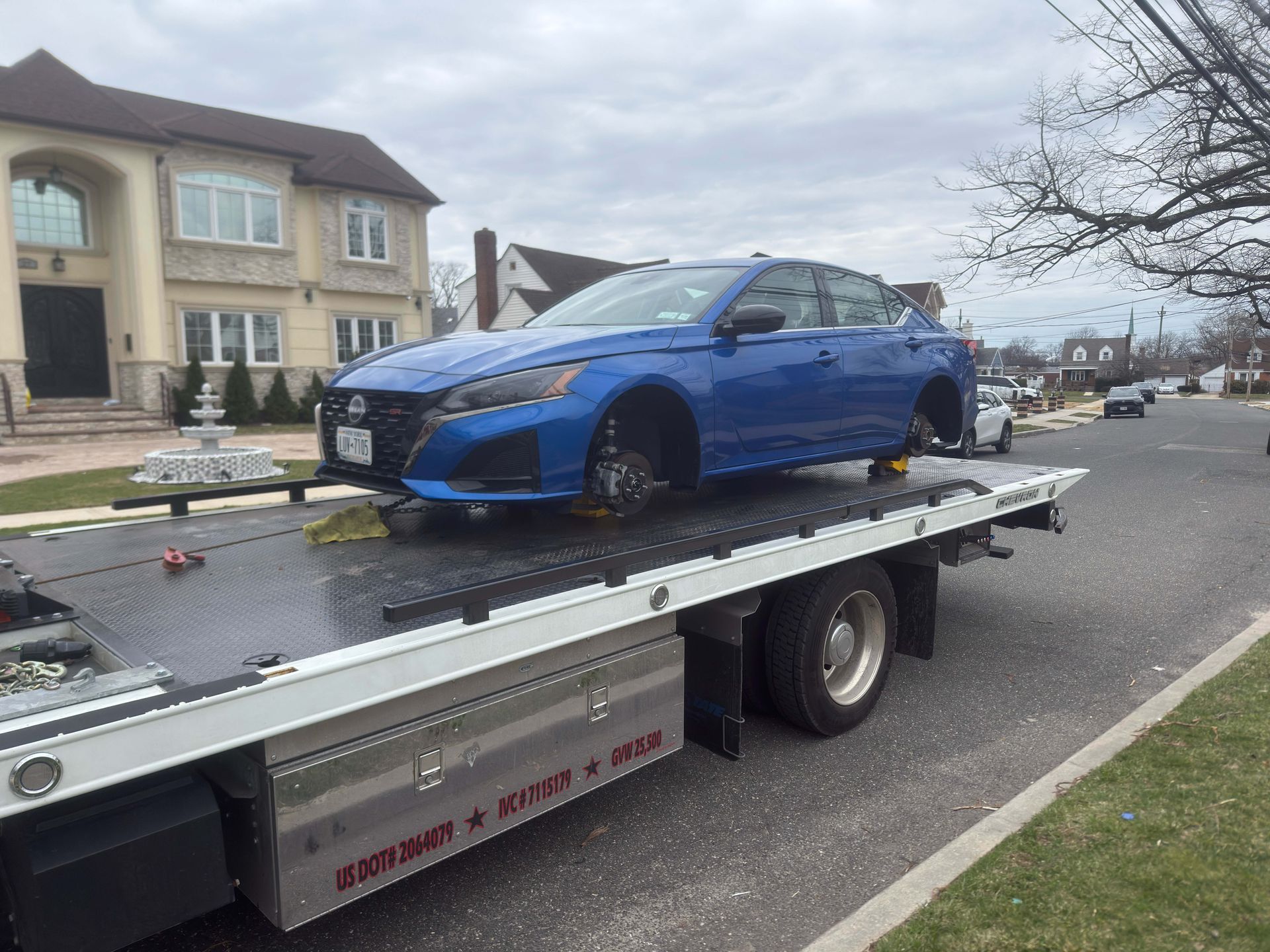 Blue sports coupe on a tow truck on a residential street.