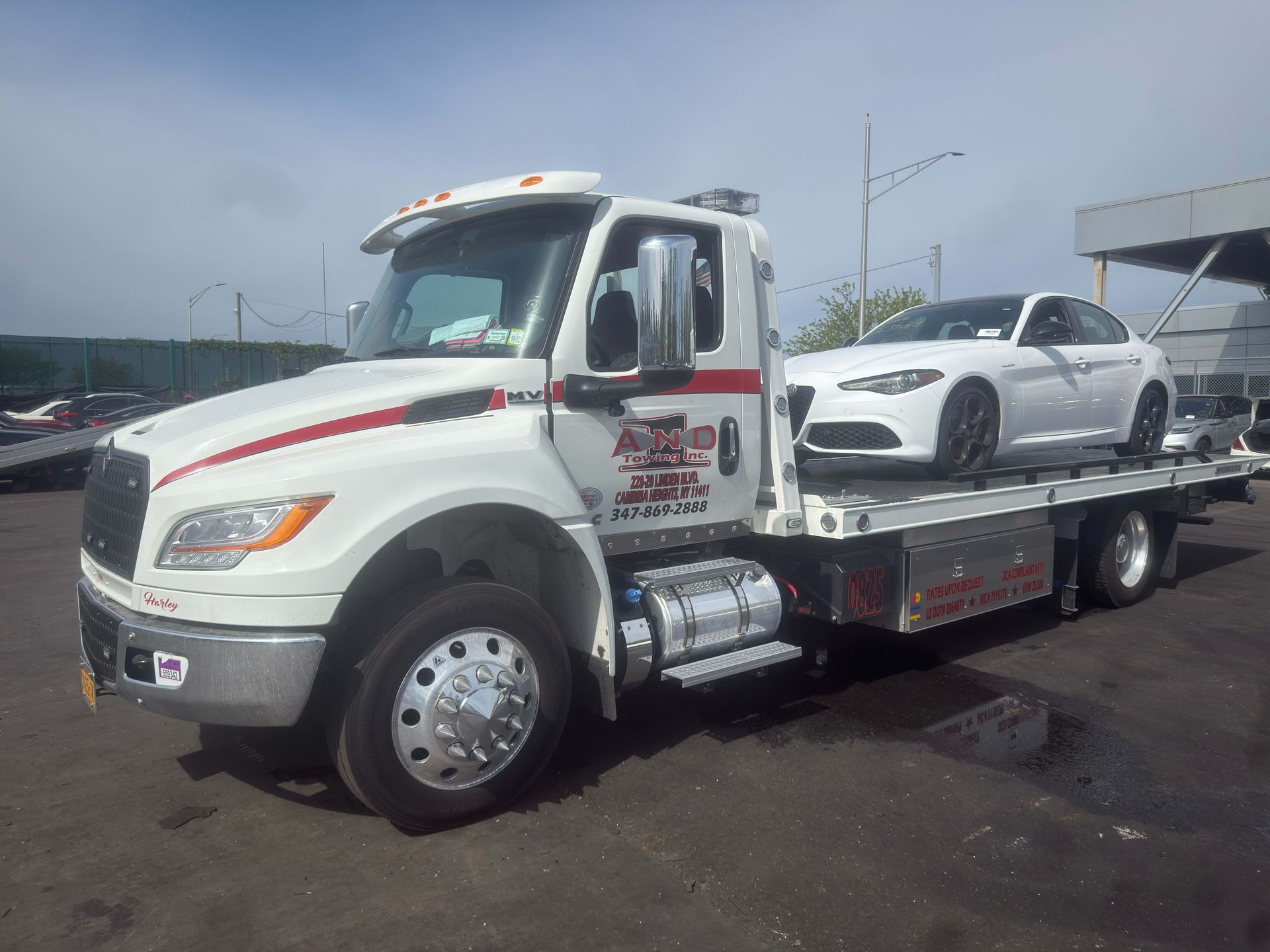 White tow truck hauling a white sedan on a flatbed in a parking lot under cloudy skies