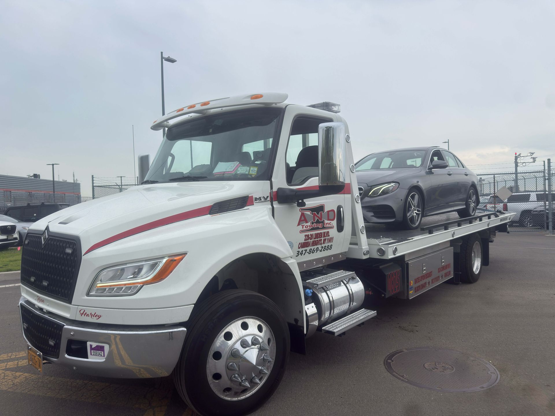 White tow truck hauling a gray car on a flatbed in an outdoor lot