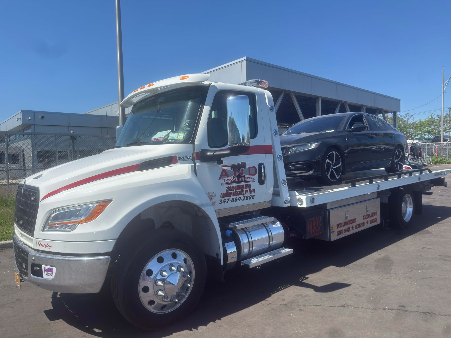 Tow truck hauling a black car on a flatbed under a clear blue sky