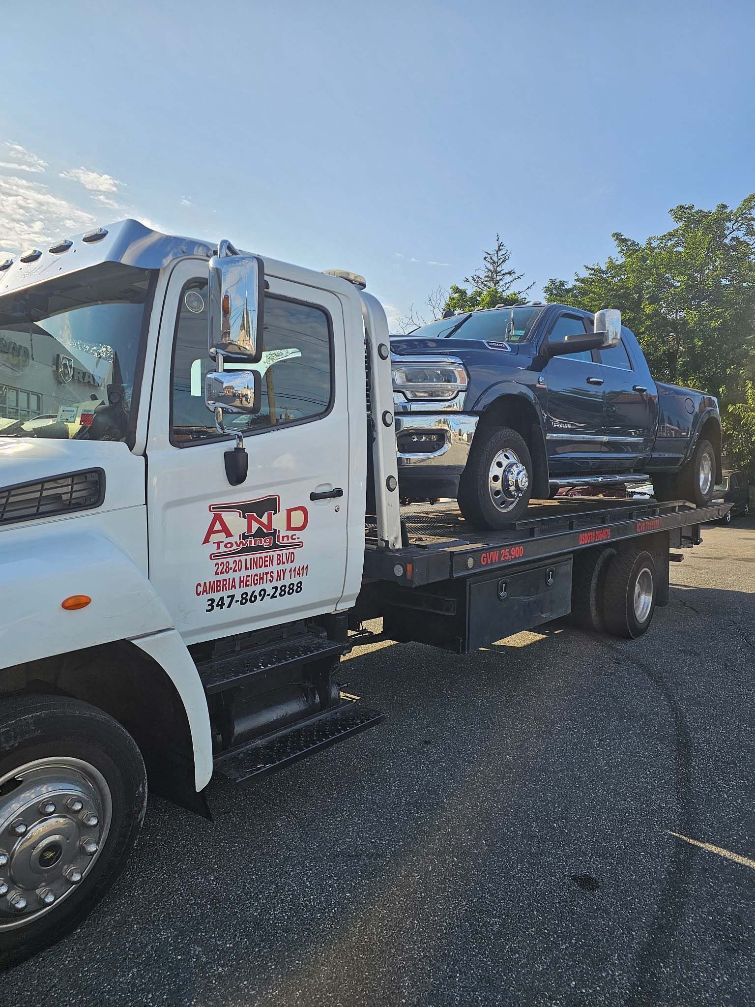 Tow truck carrying a black pickup on a flatbed in a sunny outdoor lot