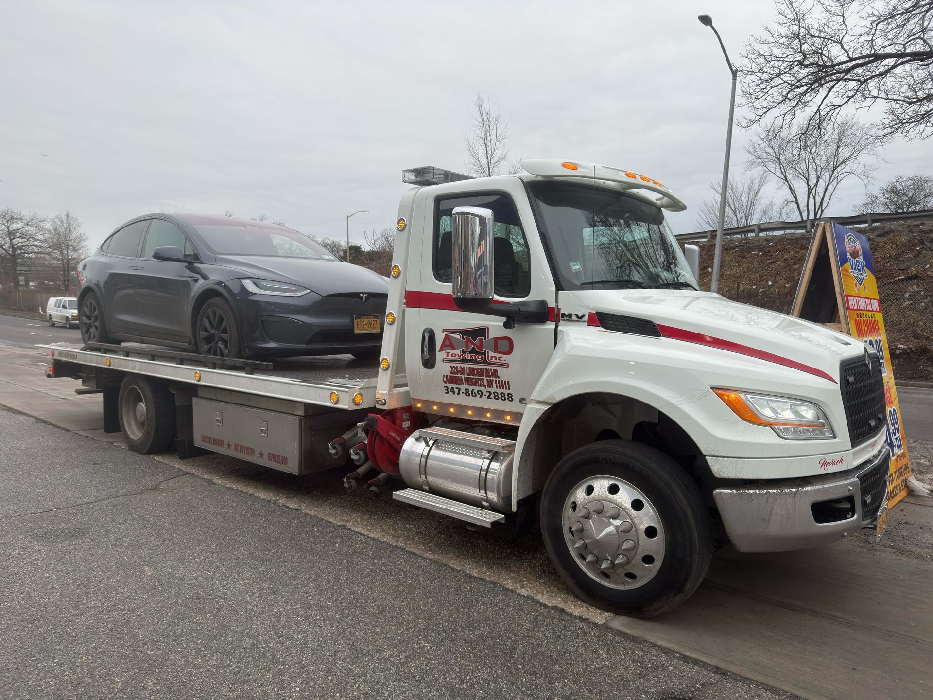 Tow truck carrying a gray car on a flatbed in a parking lot