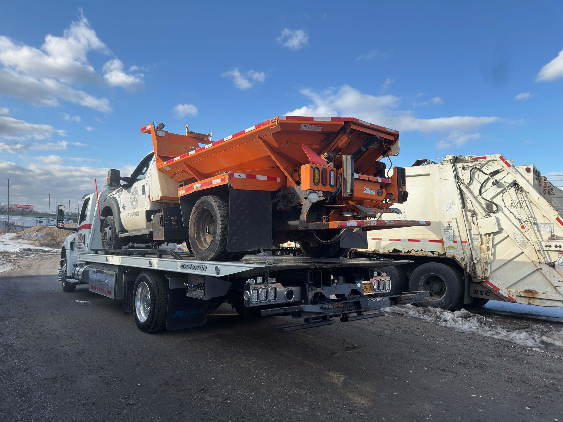 Orange construction dump truck loaded on a flatbed tow truck in a snowy lot