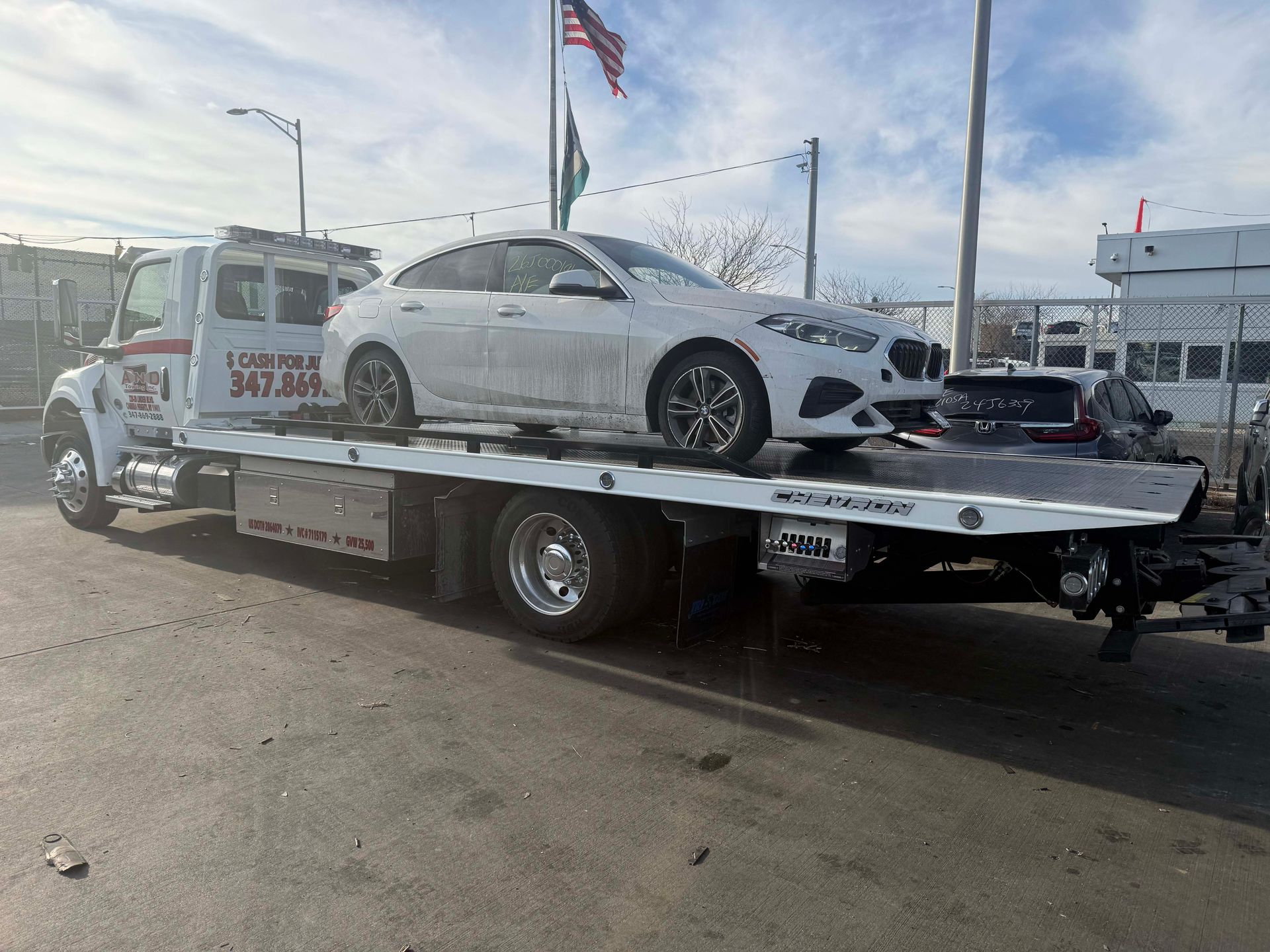 White sedan on a tow truck in a parking lot under a clear sky