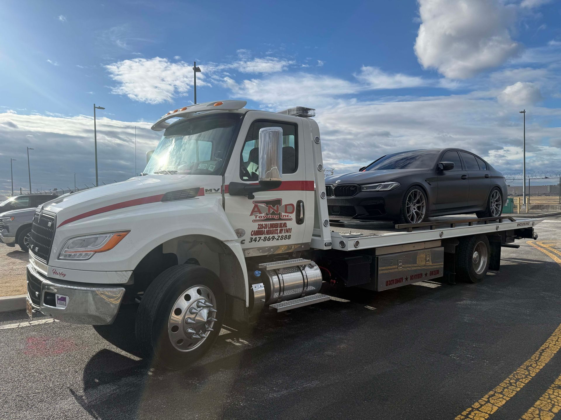 White tow truck carrying a black sports car on a flatbed under a cloudy sky
