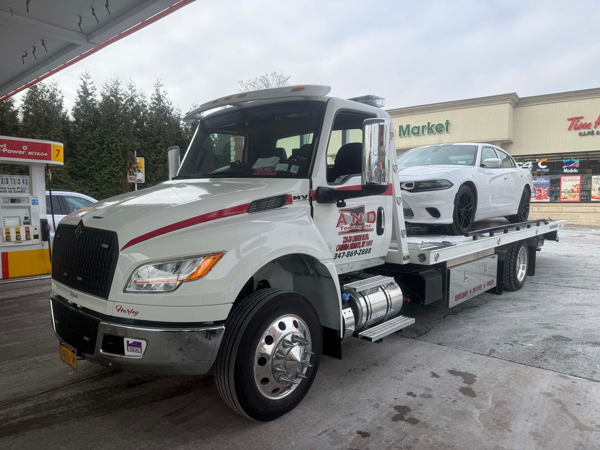 White tow truck at a gas station, carrying a white car on its flatbed.