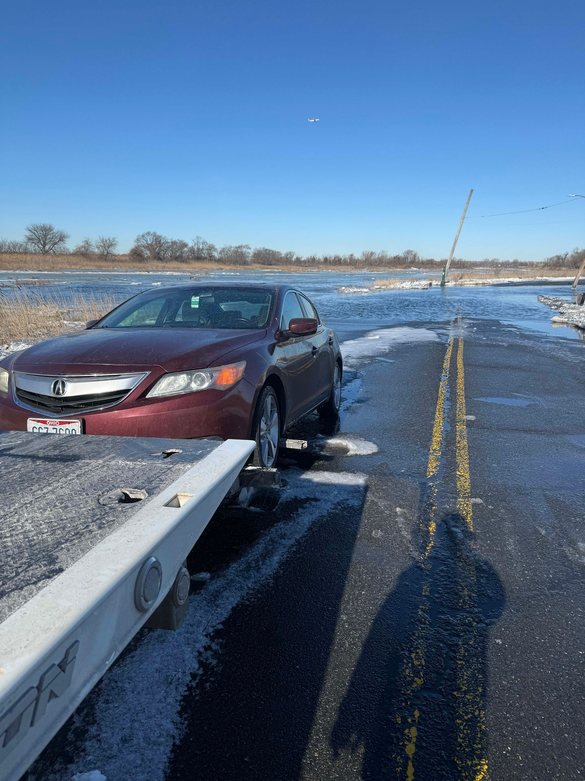 Maroon sedan stranded on a snowy rural road beside a guardrail under a clear blue sky