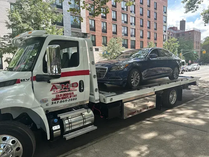 Tow truck with a blue car on its flatbed, parked on a city street.