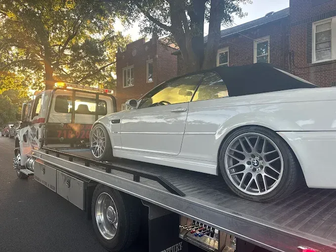White BMW convertible being towed on a flatbed tow truck on a city street.