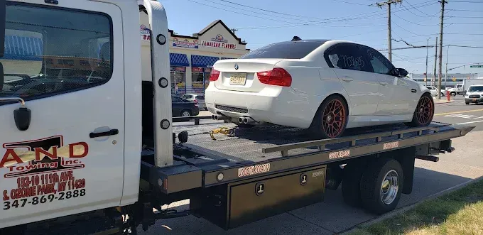 White BMW sedan being towed on a flatbed tow truck. The tow truck is white. Sunny day.
