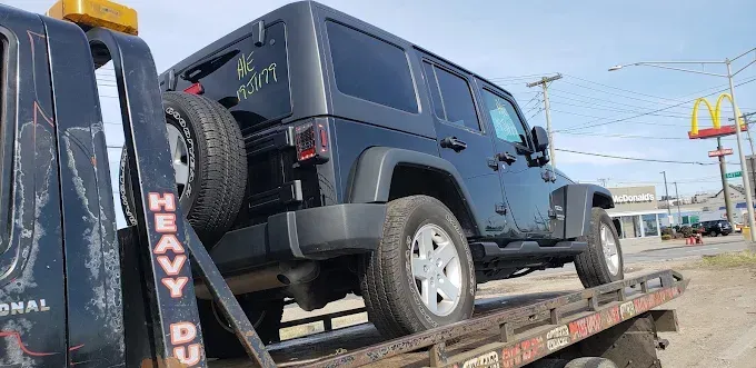 A black Jeep Wrangler on a tow truck. McDonald's sign in the background. Sunny day.