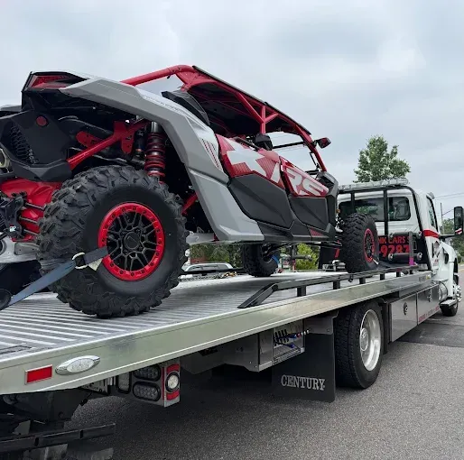 Red and gray all-terrain vehicle loaded onto a flatbed tow truck.