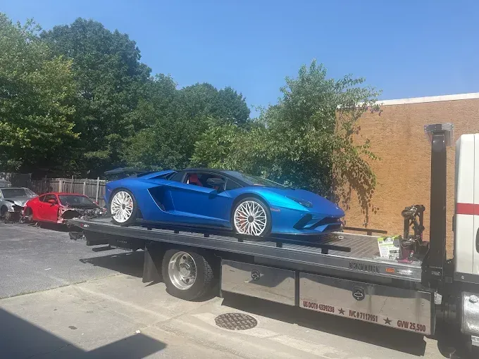 Blue Lamborghini on a flatbed tow truck outdoors on a sunny day.