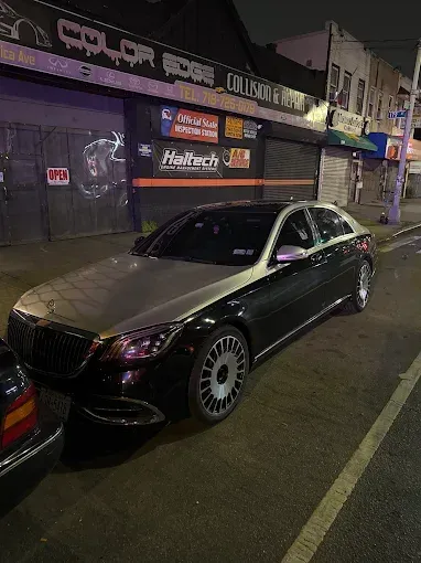 Black and silver Maybach sedan parked on a city street at night in front of a collision repair shop.