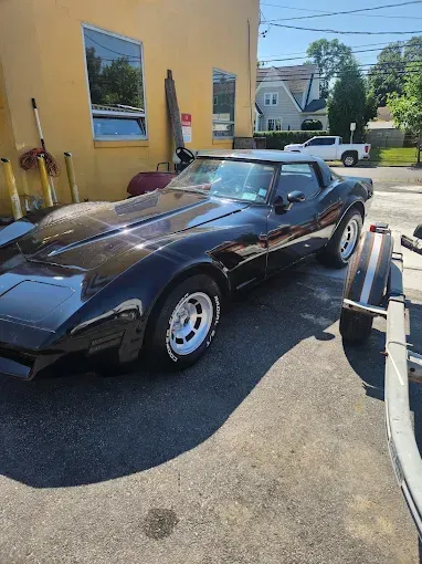 Black Corvette convertible parked outside a yellow building on a sunny day.