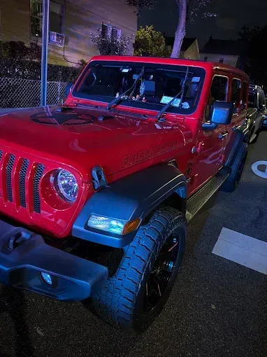Red Jeep Wrangler parked on a city street at night.