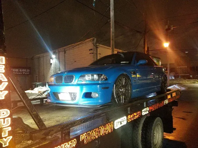 Blue sports car on a tow truck at night in a wet street, with city lights in the background