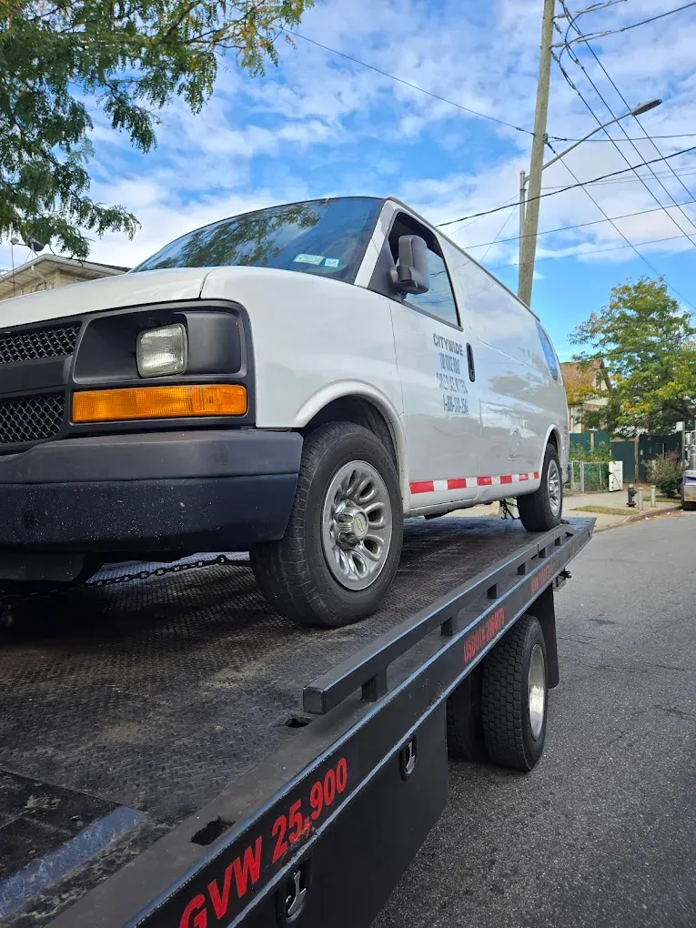 White cargo van on a flatbed tow truck on a street under a partly cloudy sky