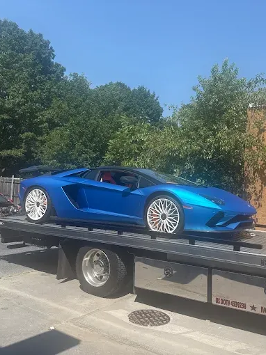 Blue sports car on a flatbed truck, parked outdoors under a sunny blue sky.