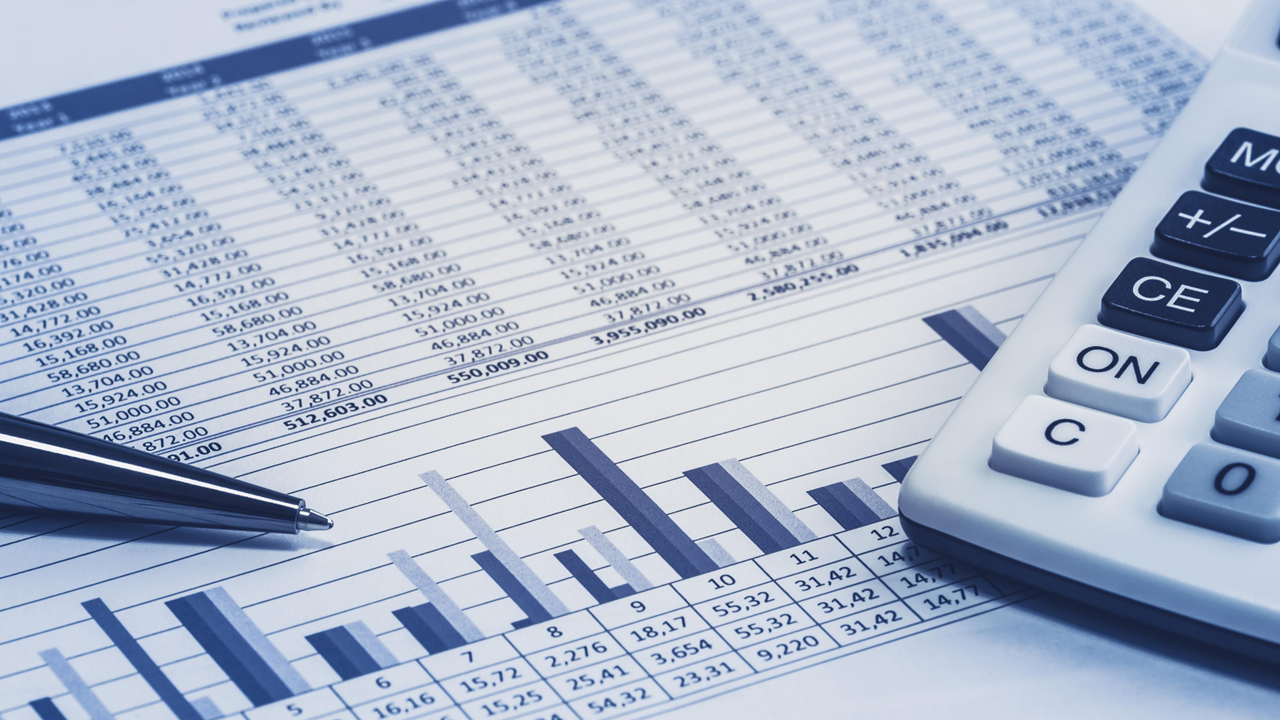 Spreadsheet, bar graph, calculator, and pen on a desk, representing financial data.