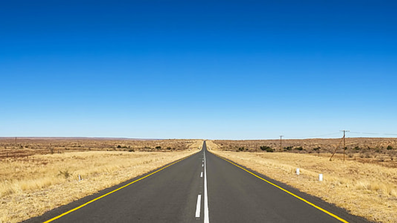 Road stretching into the distance under a clear blue sky in a desert landscape.