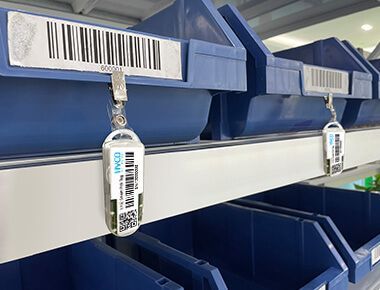 A row of blue bins on a shelf with (L102 Chargeable Wireless Light Tag) attached to them.