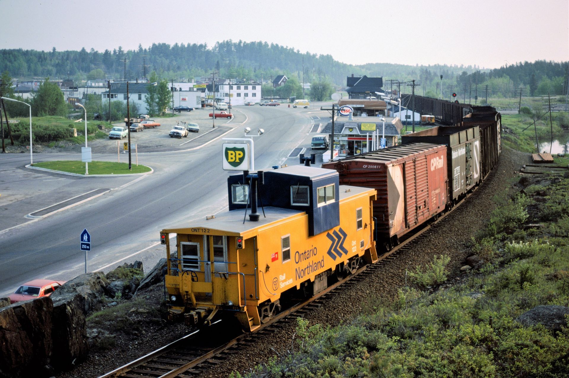 A yellow train is going down the tracks next to a bp gas station