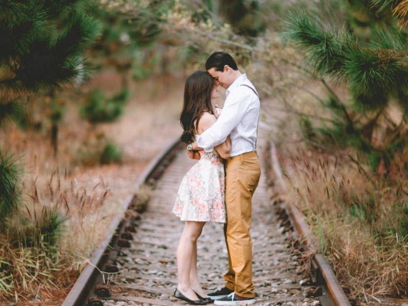 A man and a woman are kissing on train tracks.