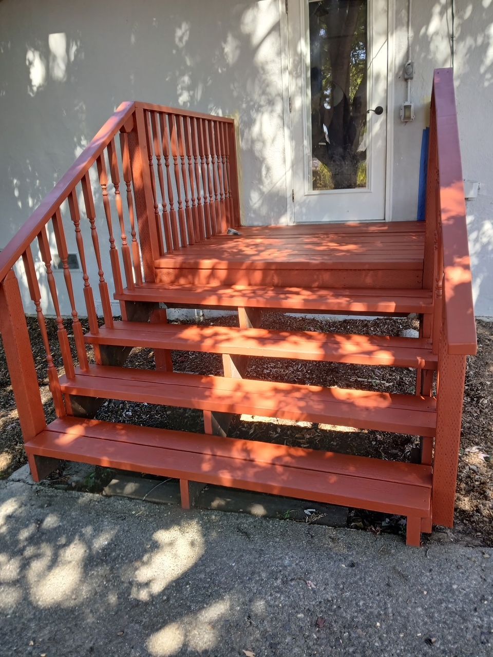  new painted Red wooden porch steps with railings beside a house and door, dappled with sunlight