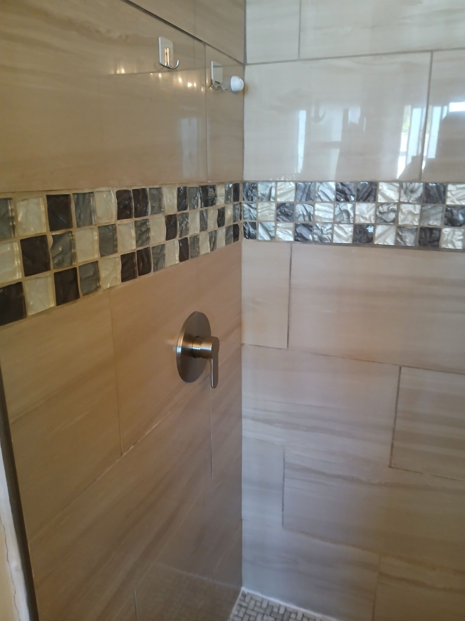 Tiled bathroom shower wall with a chrome shower control and decorative mosaic border