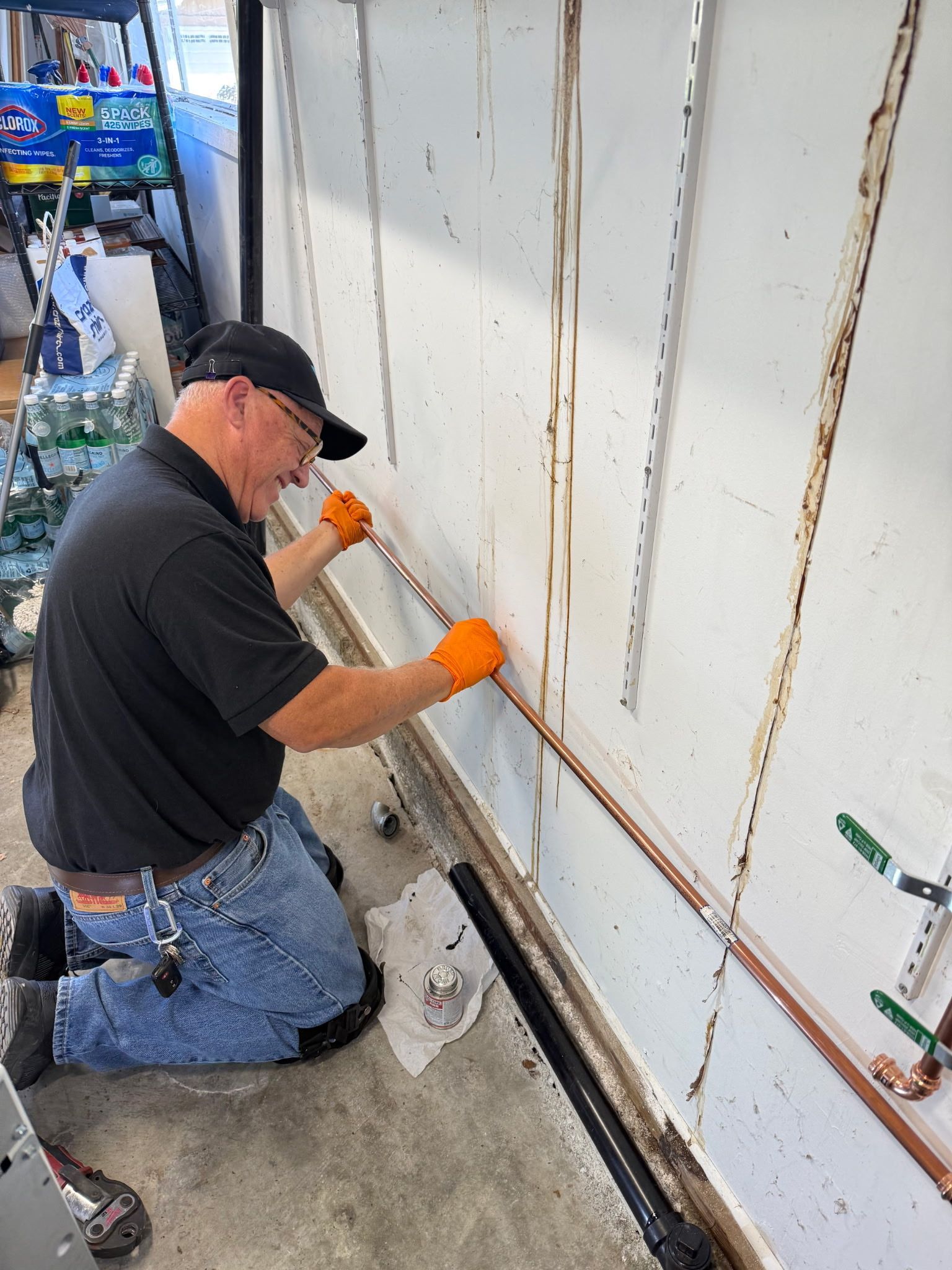 Worker in black cap and orange gloves sealing a wall joint with a caulking gun.
