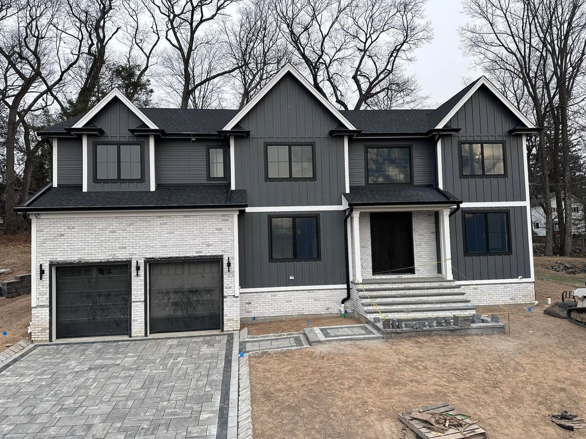 Gray two-story house with black shutters, double garage, and stone walkway in a wooded yard
