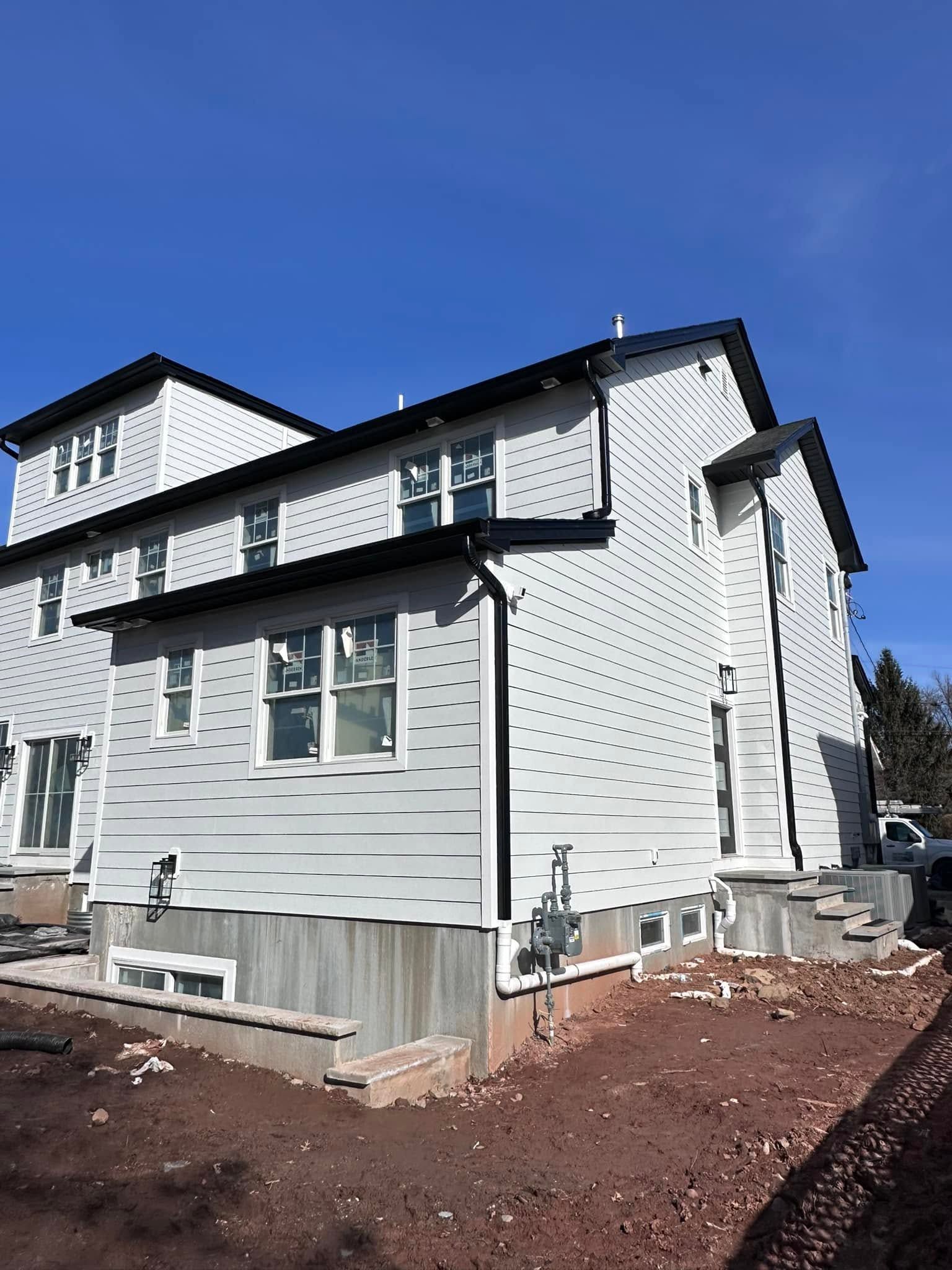 Modern white house exterior with black trim, blue sky, and bare landscaping under construction