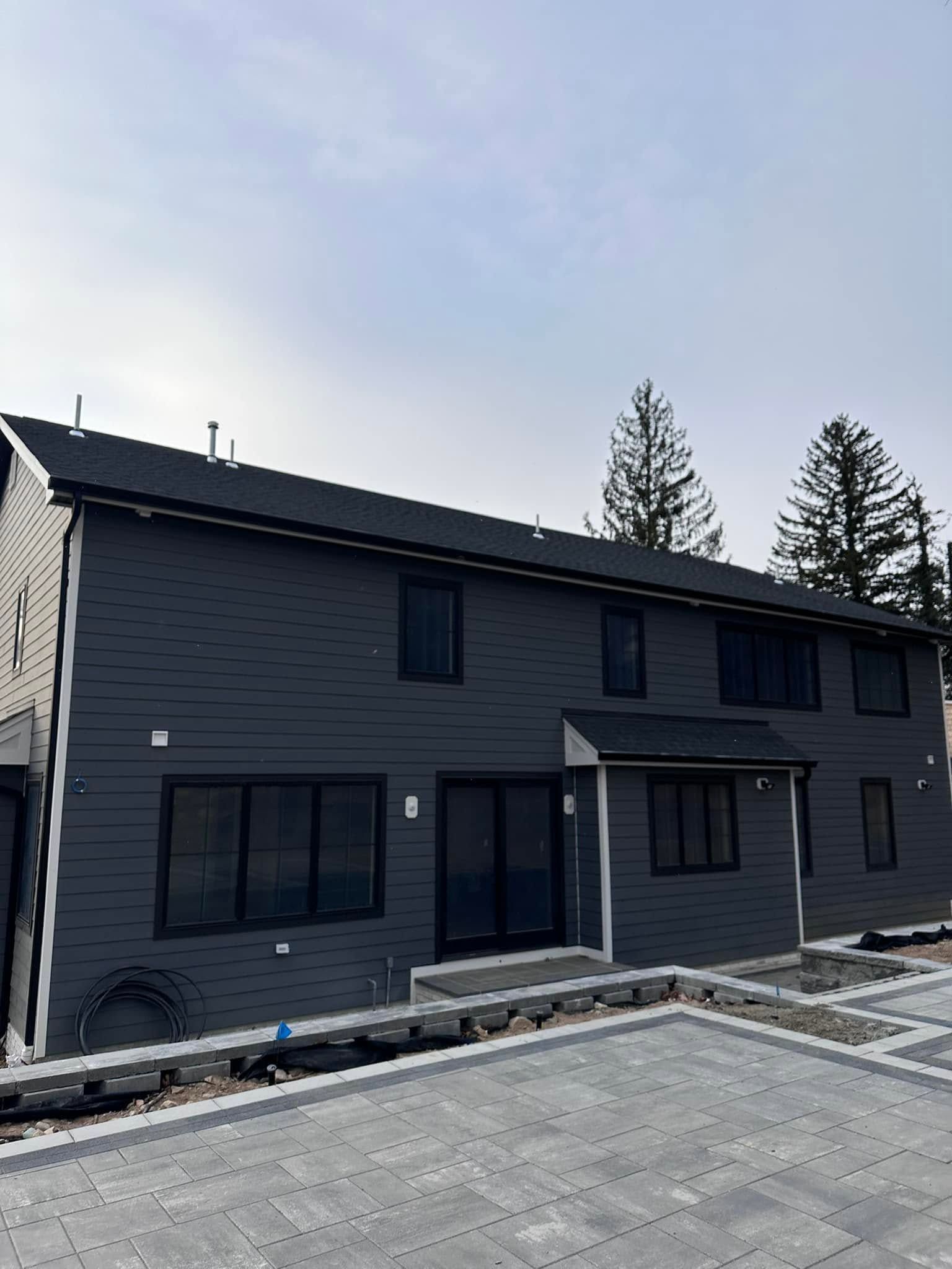 Dark gray two-story house with large windows and a front porch in a paved driveway