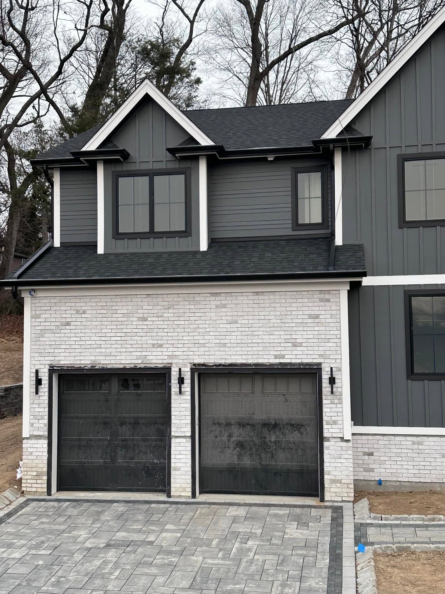 Modern two-story house exterior with gray siding, white stone garage, and double black garage doors