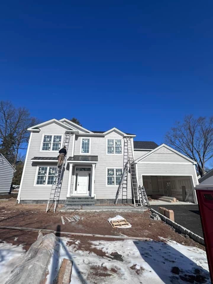 Two-story white house under construction with a person on a ladder and a snow-dusted front yard