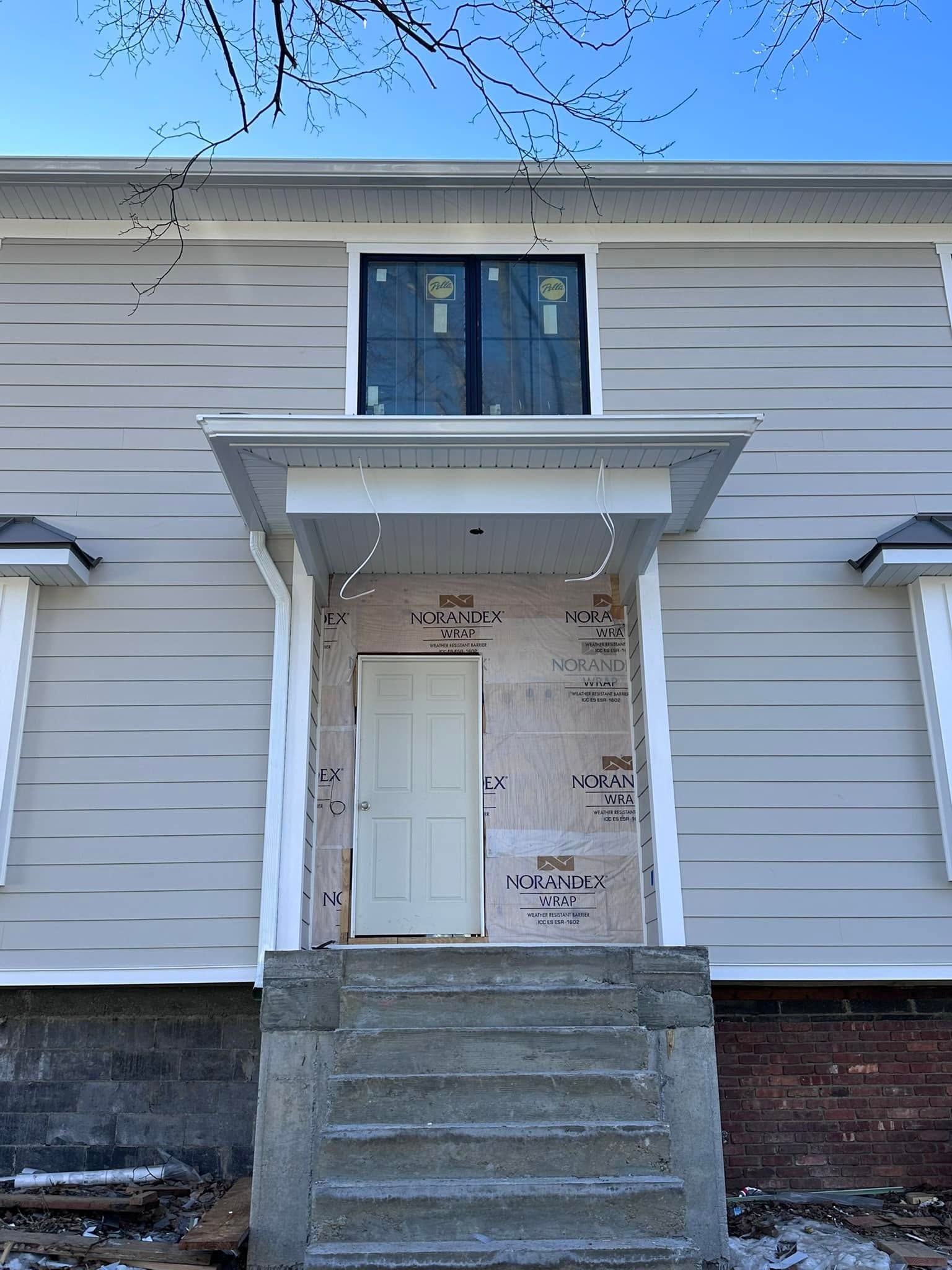 White house front entrance with concrete steps, small porch, and upper window, showing peeling paint on the doorway.