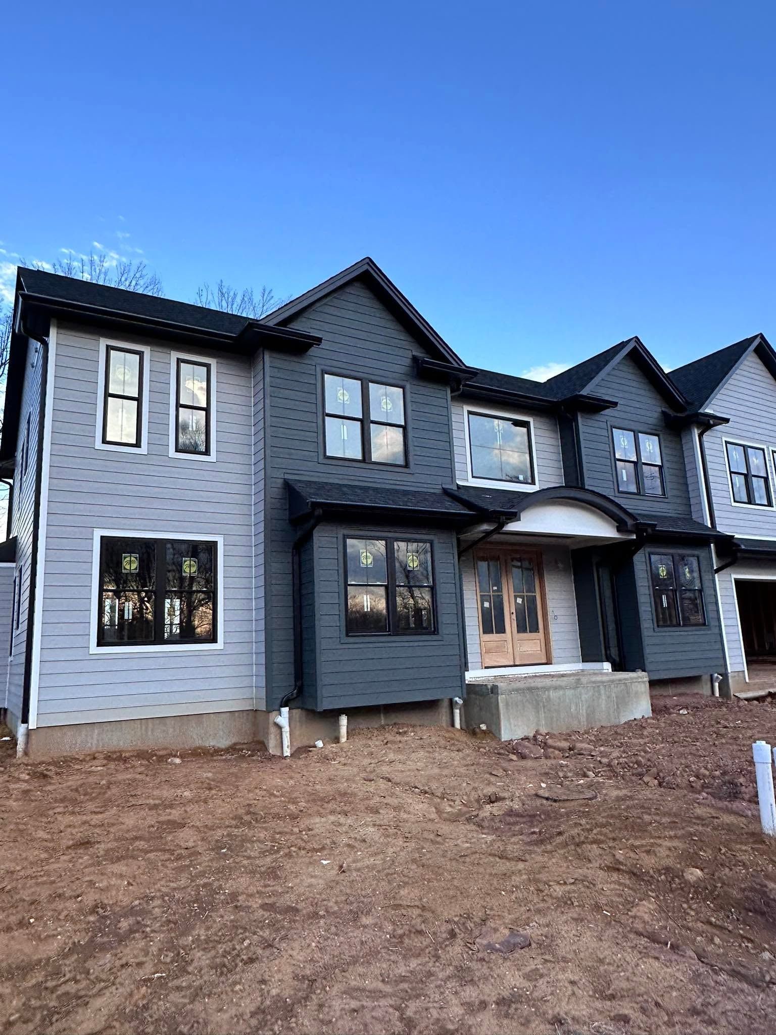 New gray two-story house under construction with bare dirt yard and clear blue sky